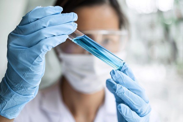 Woman holding a glass vial with blue liquid.